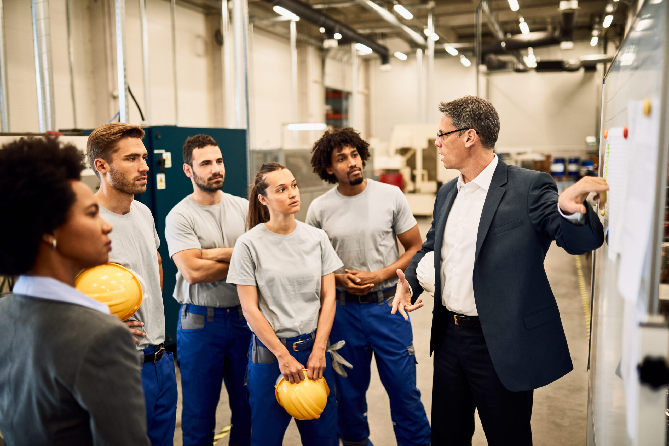 Mid adult businessman giving presentation to group of industrial workers in a factory.